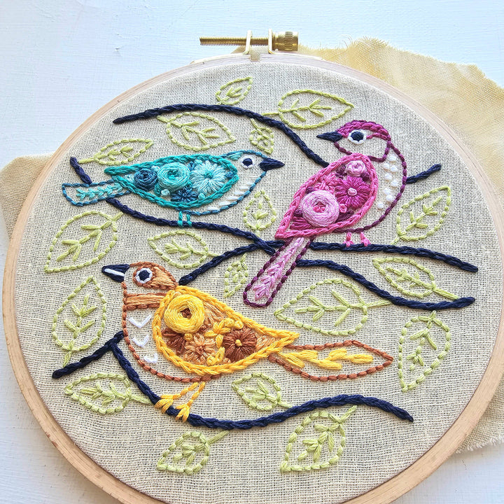 Embroidery hoop with colorful birds and leaves on a light background
