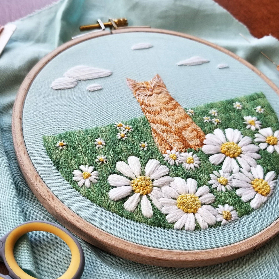 Embroidery hoop with a cat and floral design on a light blue fabric background