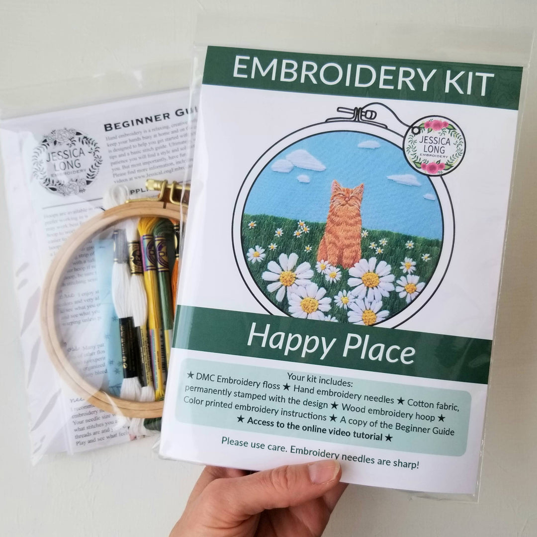 Embroidery kit with a cat and flowers design, held by a hand.