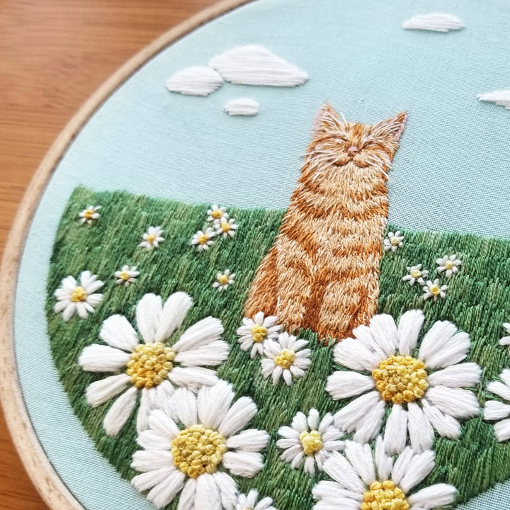 Embroidery of a cat sitting among flowers in an embroidery hoop.
