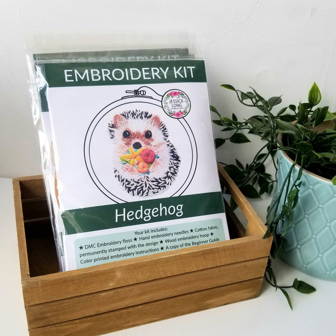Embroidery kit for hedgehog design in a wooden box with a plant in the background