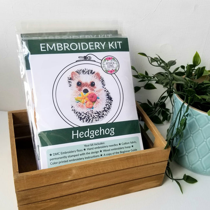 Embroidery kit for hedgehog design in a wooden box with a plant in the background