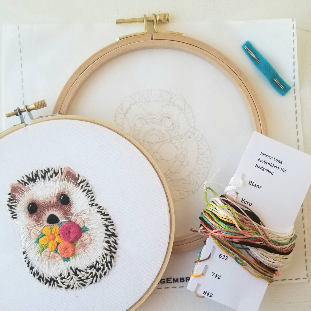 Embroidery hoop with a completed hedgehog design and embroidery kit on a white background