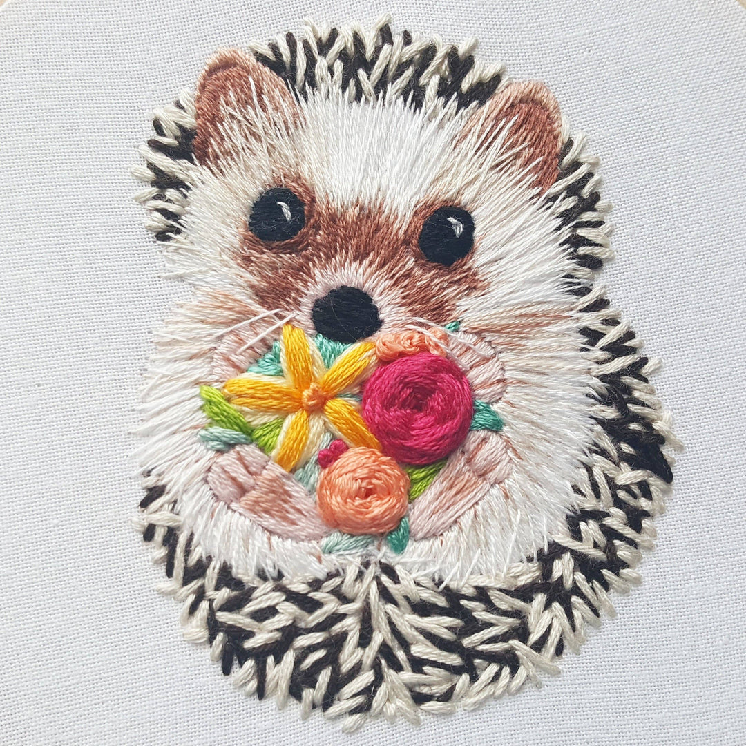 Embroidered patch of a hedgehog with flowers on a light gray background