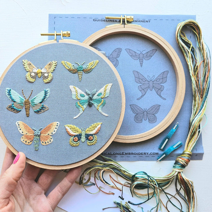 Embroidery hoop with embroidered butterflies on a blue fabric, held by a hand.