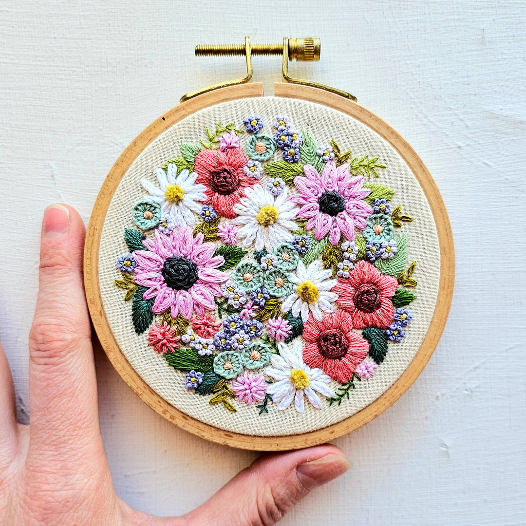 Embroidery hoop with floral design held by a hand on a light background