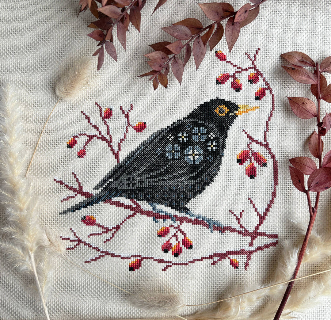 Cross-stitched bird on a branch with berries and leaves on fabric
