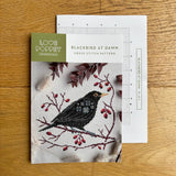 Cross stitch pattern for 'Blackbird at Dawn' by Love Poppet on a wooden surface