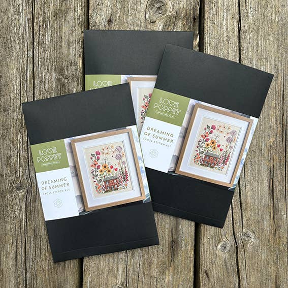Three cross-stitching kits from Love Poppy on a wooden surface