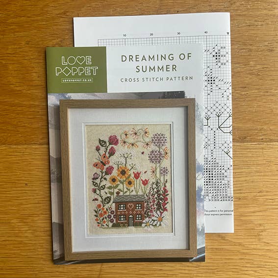 Cross stitch kit with framed design and pattern sheet on a wooden surface