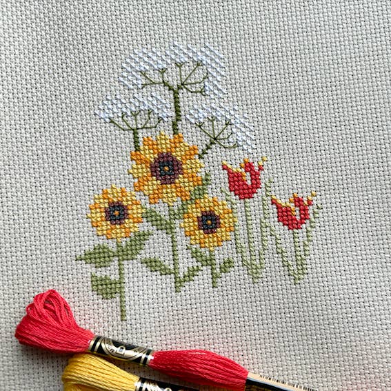 Cross-stitched flowers on fabric with embroidery floss and needle.