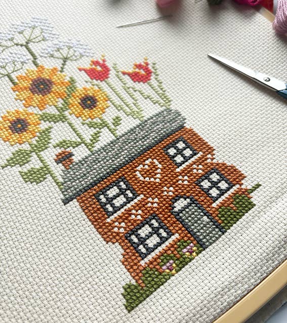 Cross-stitched house with flowers on a white fabric background