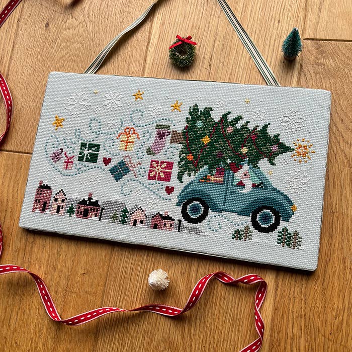 Cross-stitched design of a truck with a Christmas tree on a wooden surface