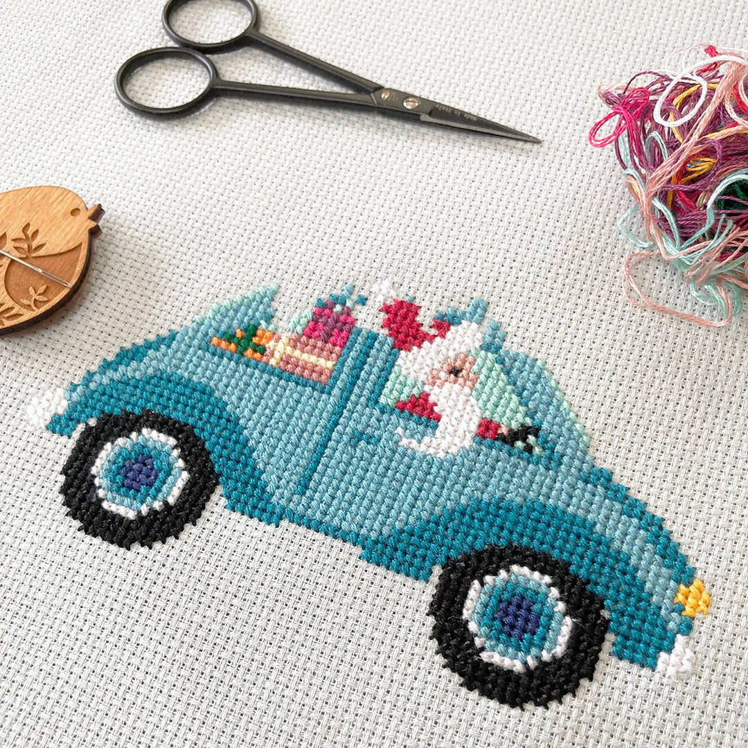 Cross-stitched blue truck with a cat and Easter eggs on fabric with scissors and thread.