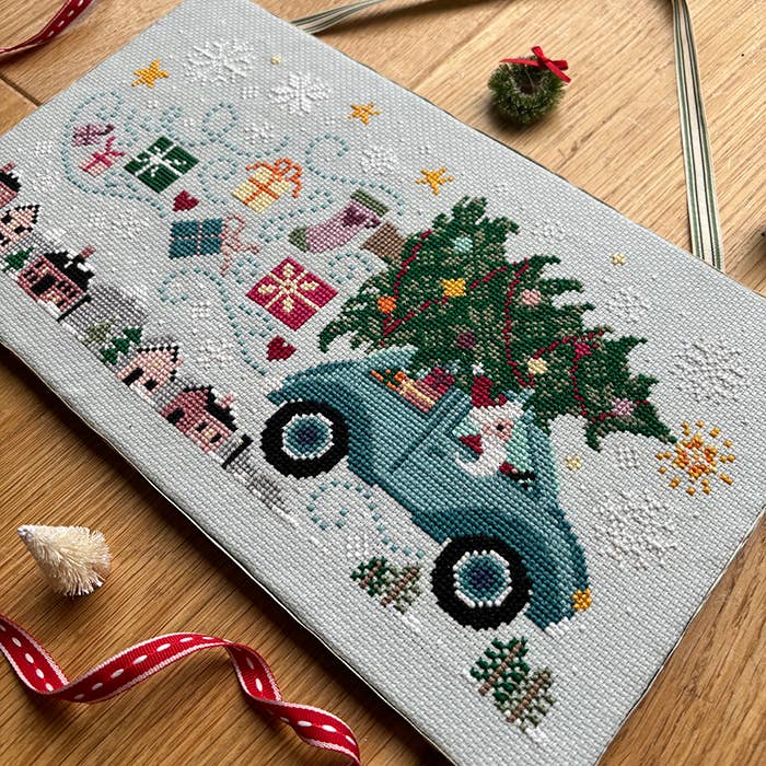 Cross-stitched design of a vintage truck with a Christmas tree on a wooden surface.