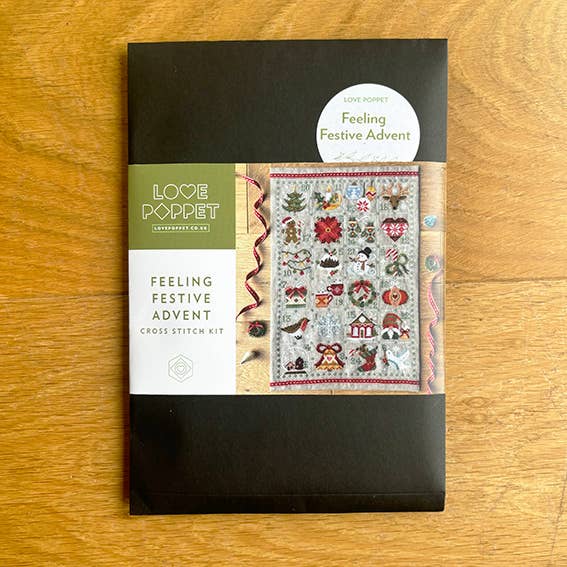 Cross stitch kit packaging with 'Love Poppet' branding on a wooden surface