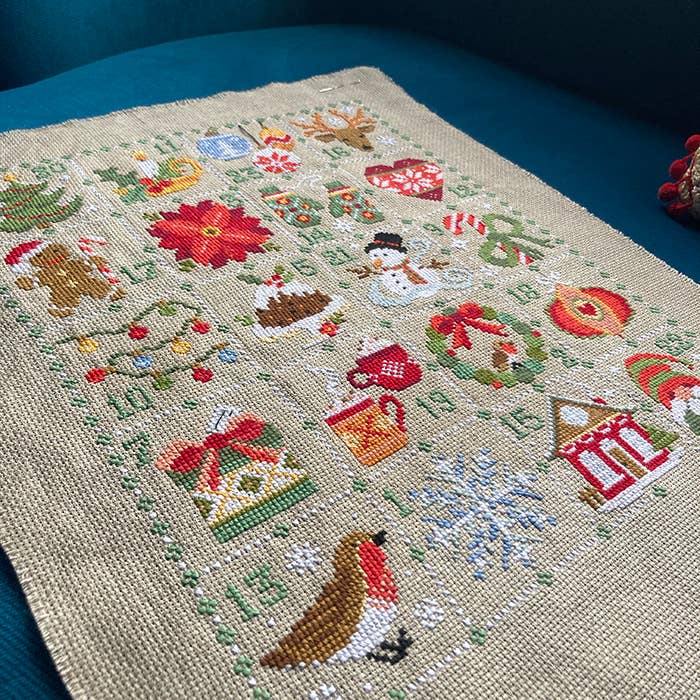 Cross-stitched Christmas-themed fabric with various festive elements on a blue surface.