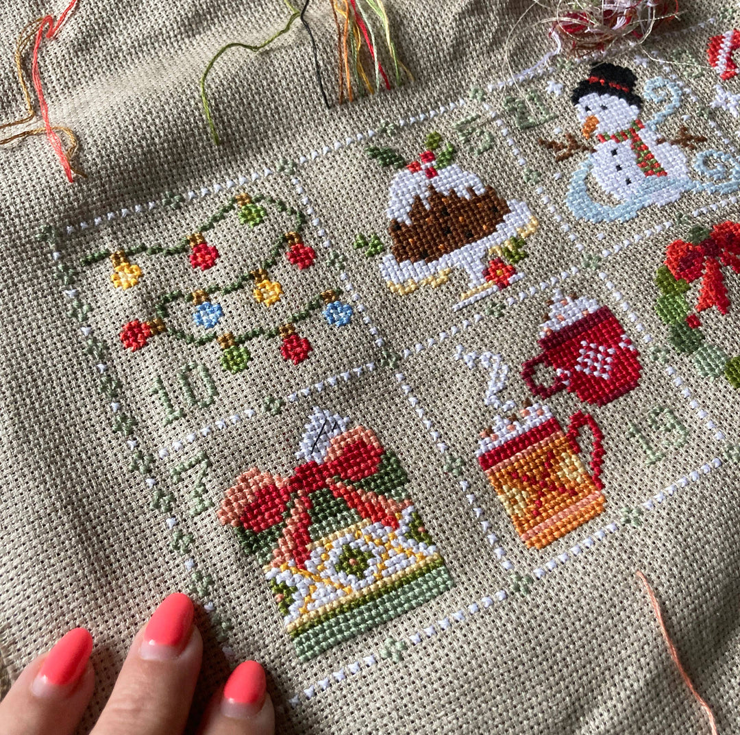 Cross-stitched Christmas-themed design on fabric with a hand holding the fabric.