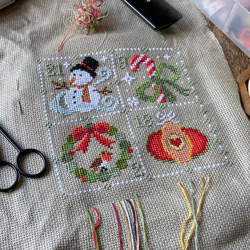 Cross-stitched snowman design on fabric with embroidery tools nearby