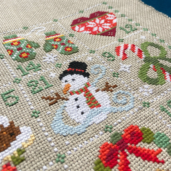 Cross-stitched snowman design with Christmas elements on fabric