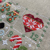Close-up of a cross-stitched piece with festive designs on beige fabric.