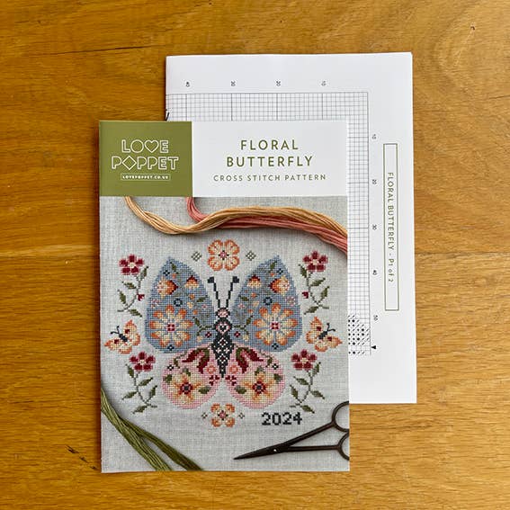 Floral butterfly cross stitch pattern with a scissor and thread on a wooden surface