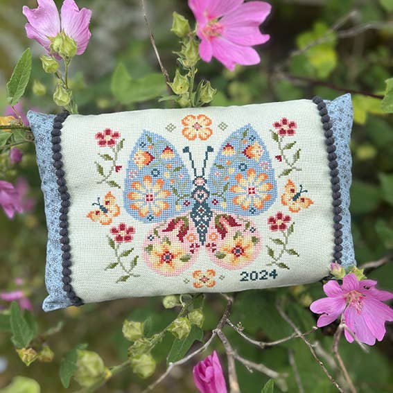 Decorative pillow with floral butterfly design and year '2024' on a green background with pink flowers.