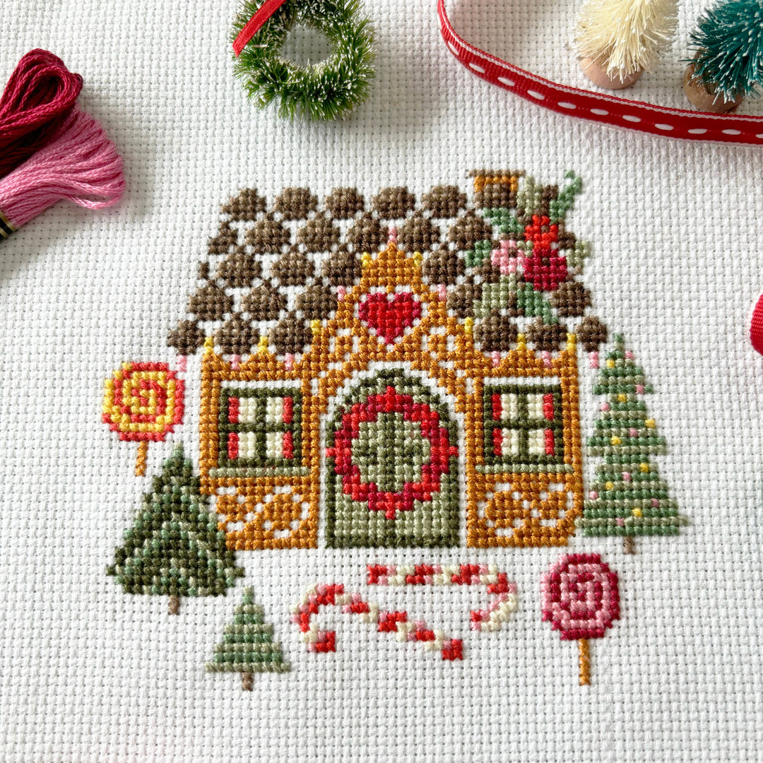 Cross-stitched gingerbread house with decorative elements on a white fabric background