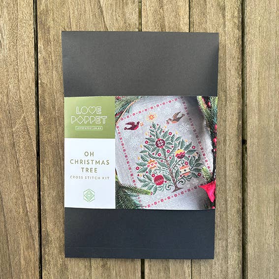 Cross stitch kit packaging with 'Love Poppet' branding on a wooden surface