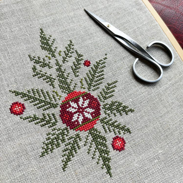 Cross-stitched design with red and green details on fabric, accompanied by a pair of scissors.