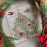 Embroidered Christmas tree design with festive elements on fabric, surrounded by greenery and berries.