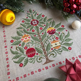 Cross-stitched Christmas tree design on fabric with festive decorations around.