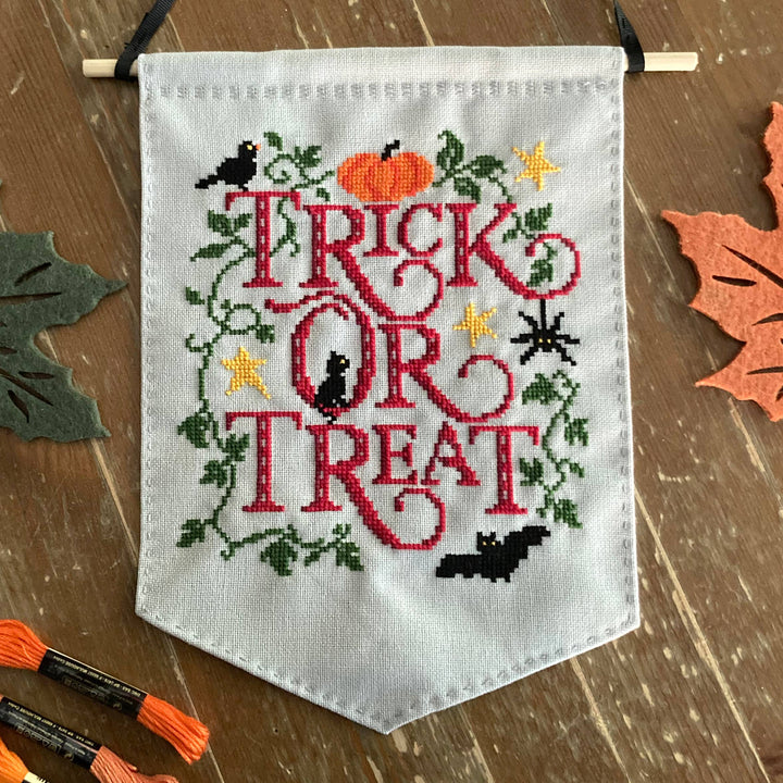 Embroidered banner with 'Trick or Treat' text on a wooden surface with Halloween decorations.