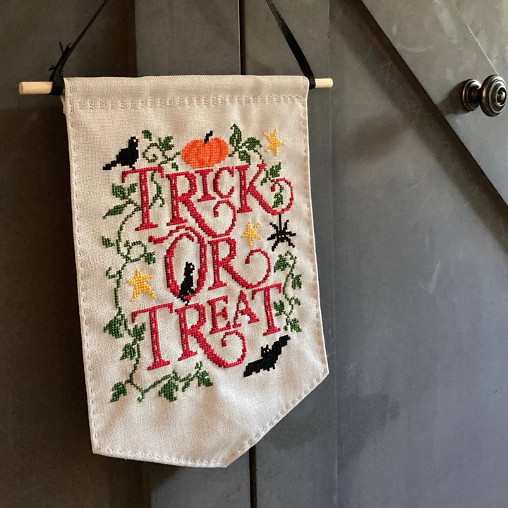 Embroidered banner with 'Trick or Treat' text hanging on a door.