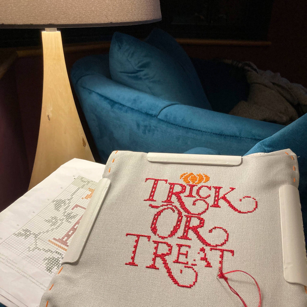 Embroidered 'Trick or Treat' design on a fabric with a blue couch in the background.