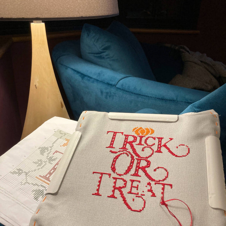 Embroidered 'Trick or Treat' design on a fabric with a blue couch in the background.