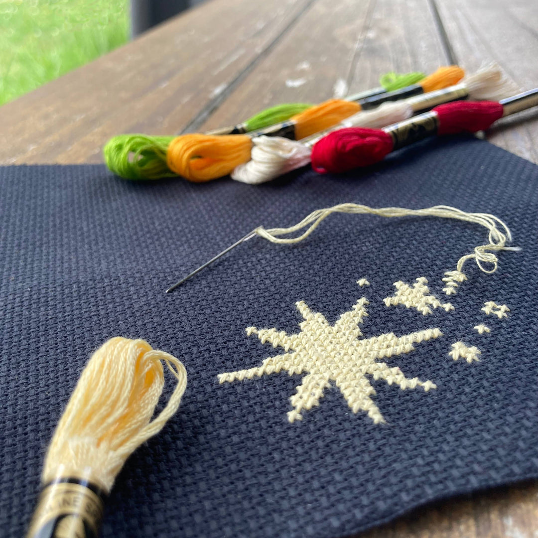 Embroidery work in progress with colorful threads and a partially completed design on dark fabric.