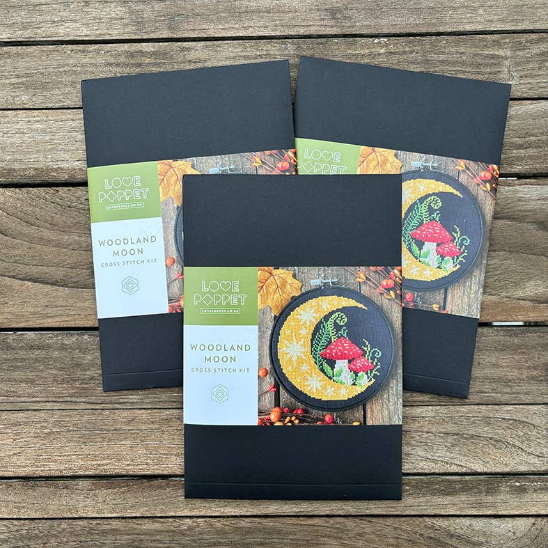 Three needlework kits with 'Woodland Moon' design on a wooden surface