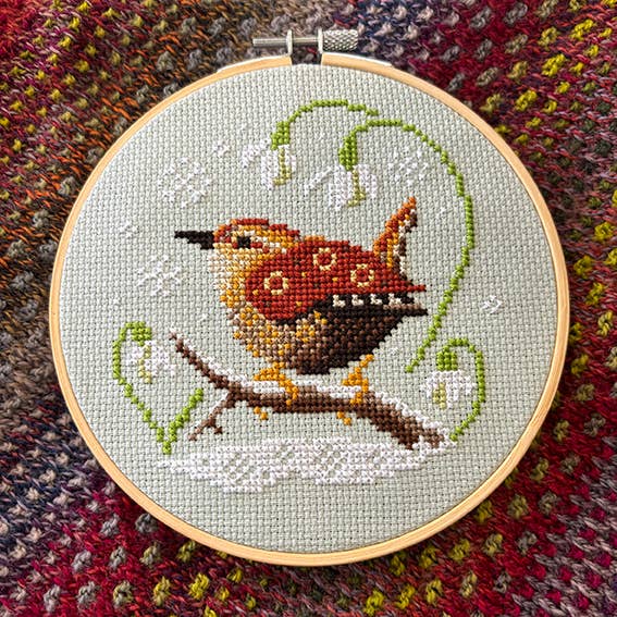 Embroidery hoop with a cross-stitched wren on a textured fabric background