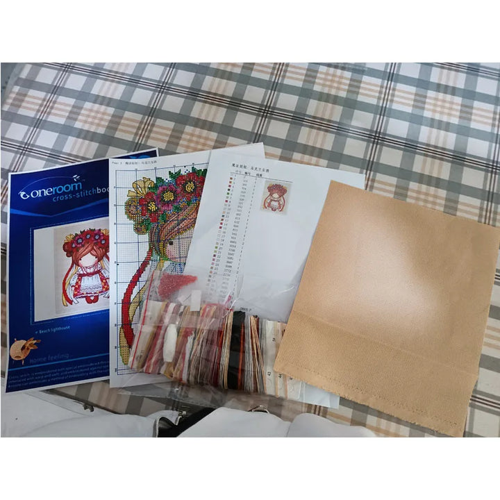 Cross-stitching supplies including a pattern book, fabric, and other materials on a plaid surface.