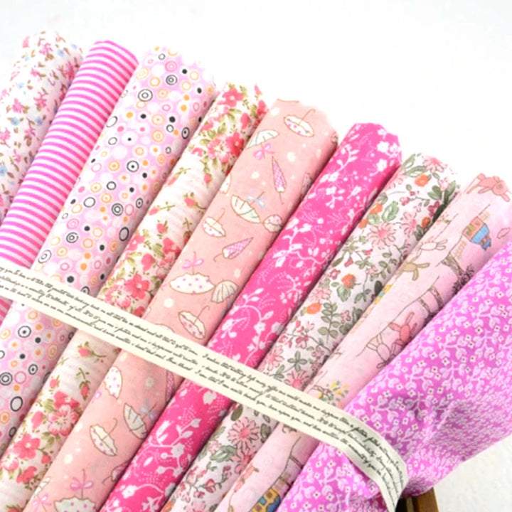 Collection of pink fabric rolls with various patterns tied together on a white background