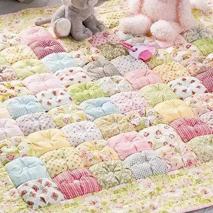 Pastel-colored quilt with various patterns and textures, featuring soft toys on top.
