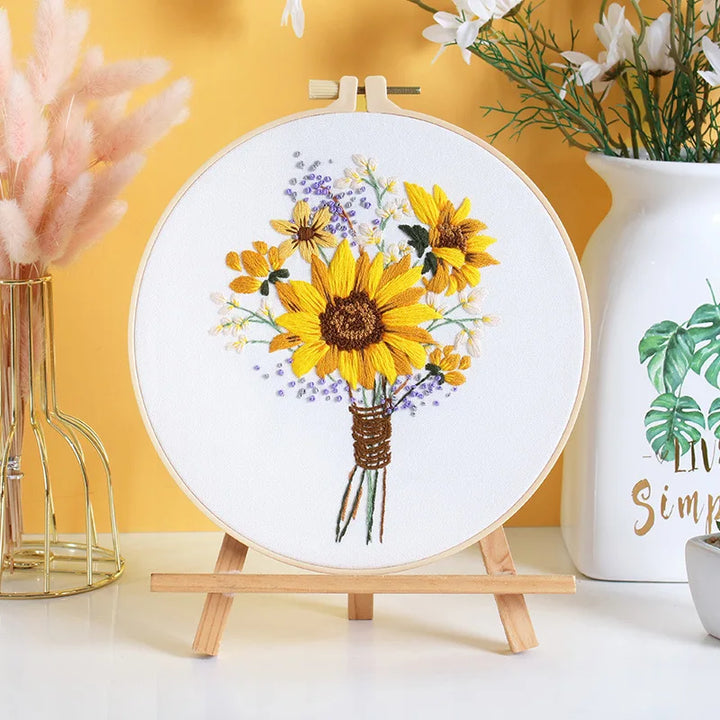 Embroidery hoop with sunflower design on a white surface with decorative elements.