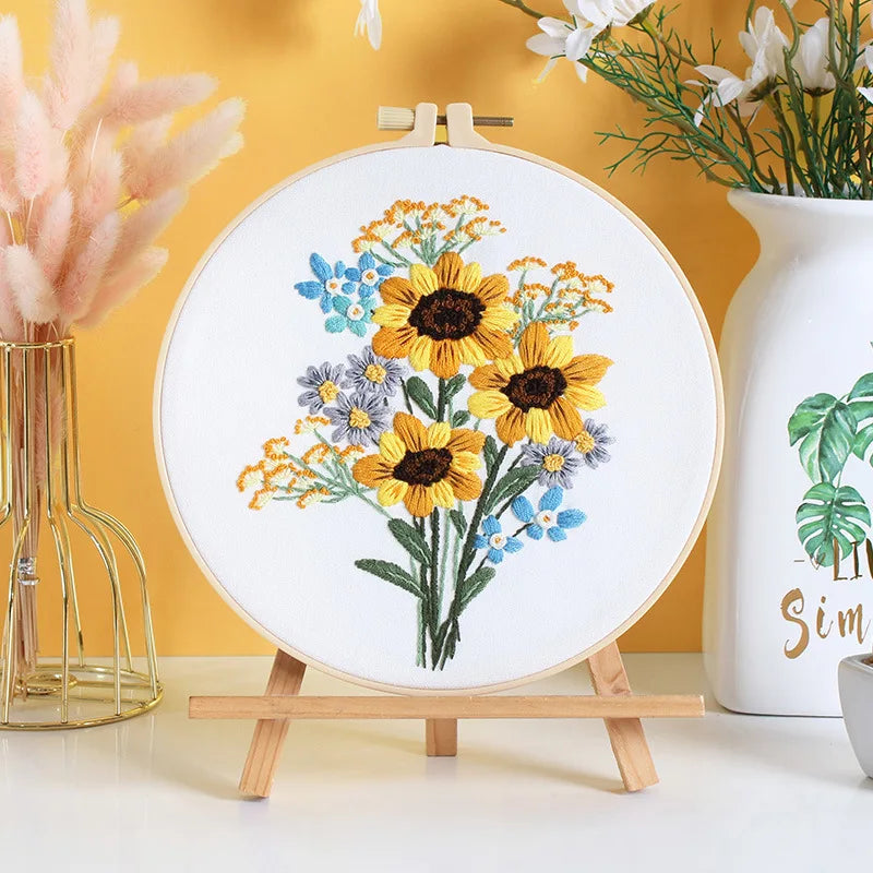 Embroidery hoop with floral design on a stand against a yellow wall with decorative elements.
