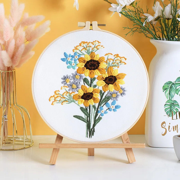Embroidery hoop with floral design on a stand against a yellow wall with decorative elements.