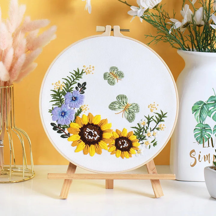 Embroidery hoop with floral design on a stand against a yellow wall.
