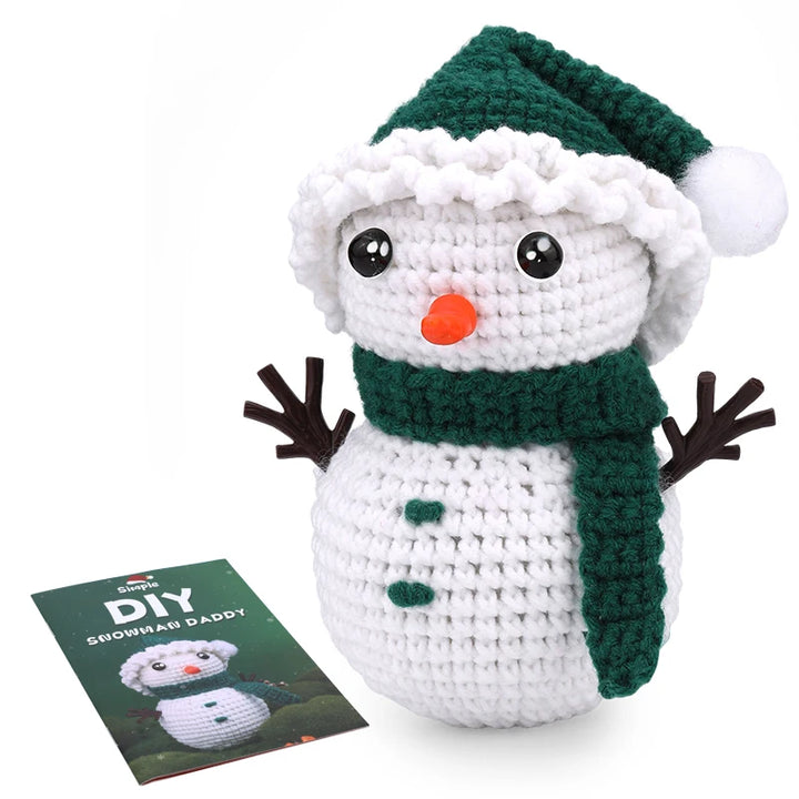 Crocheted snowman toy with green scarf and hat, next to a DIY craft book on a white background