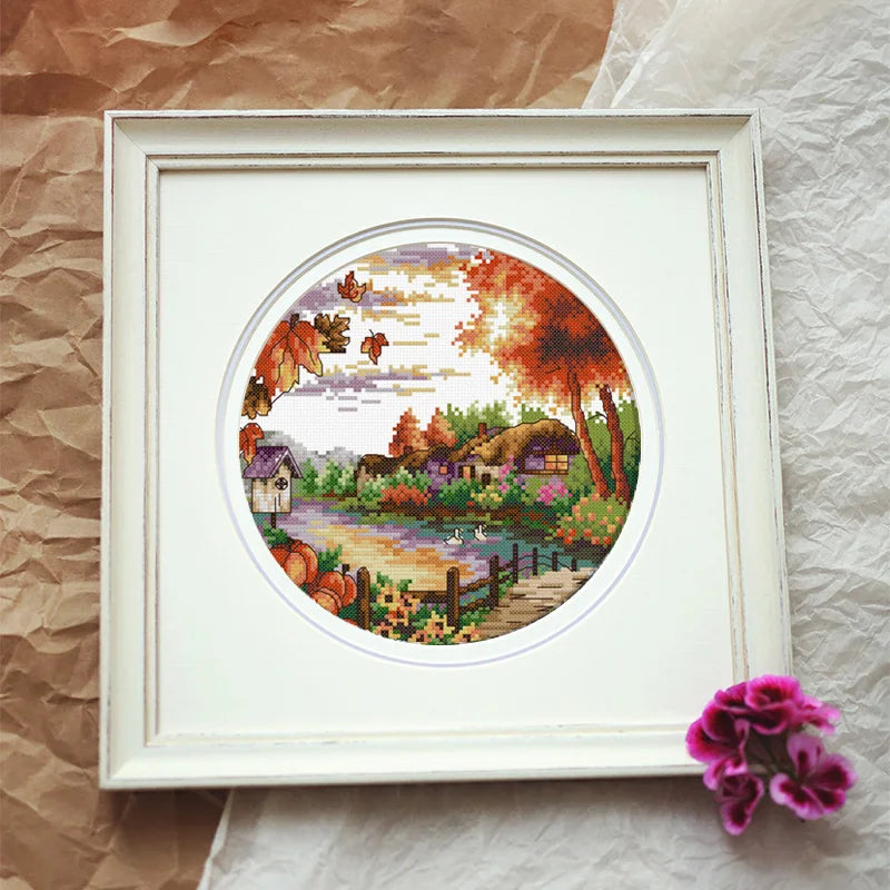 Framed cross-stitched landscape with autumn theme on a textured surface.