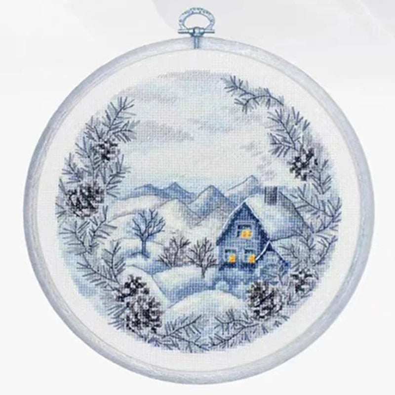 Cross-stitched winter scene with a house and snowy landscape in an embroidery hoop.