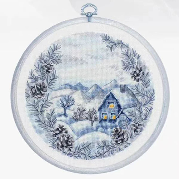 Cross-stitched winter scene with a house and snowy landscape in an embroidery hoop.